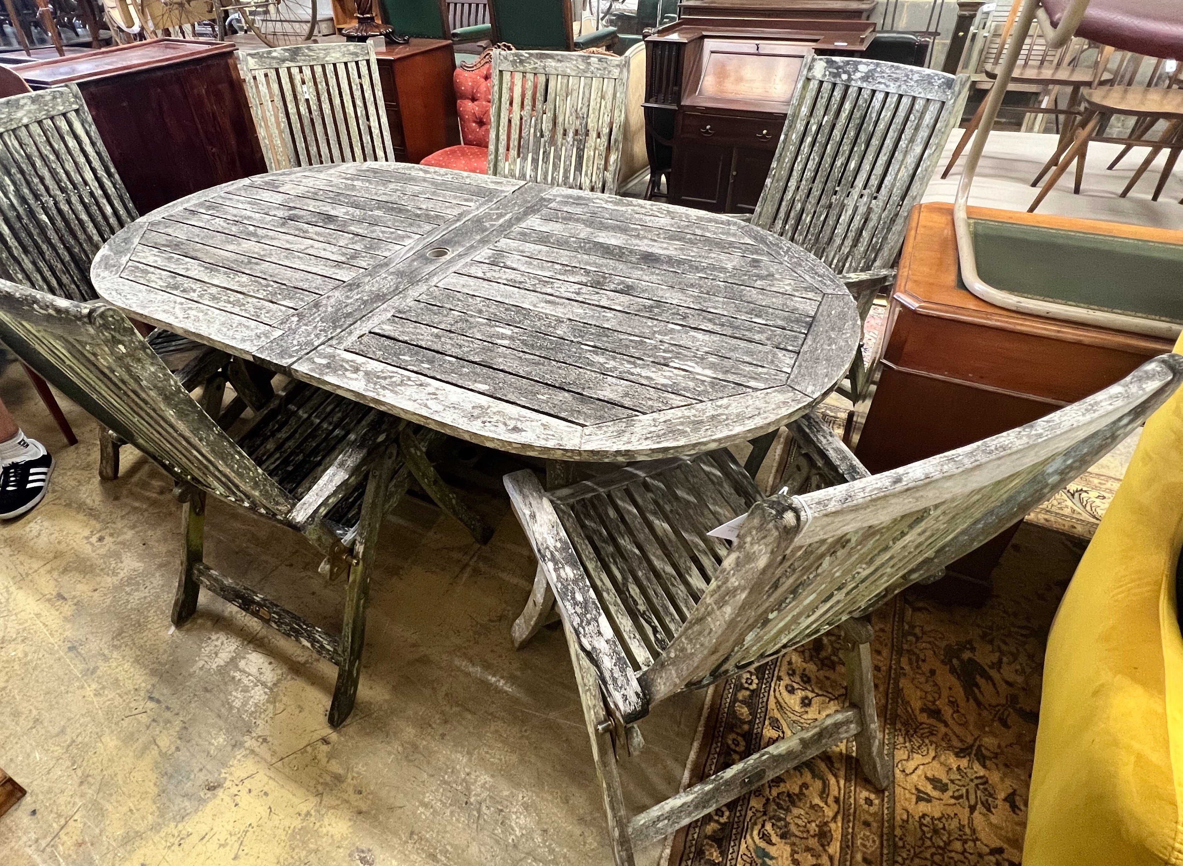 A weathered teak oval extending garden table, extended 250cm width 109cm height 73cm, and six folding garden elbow chairs